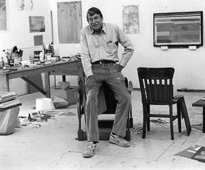 Black-and-white photograph of Richard Diebenkorn in his studio surrounded by supplies and his art